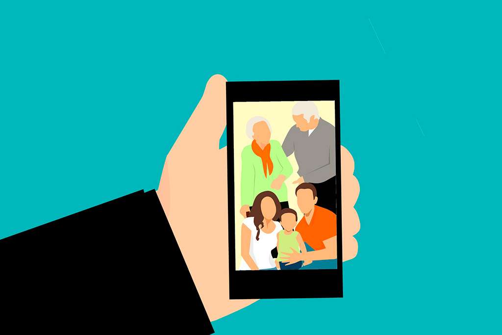 Puedes ver una mano sosteniendo un smartphone donde se puede ver la imagen de una familia: padre, madre, un niño pequeño y sus abuelos. El envío de imágenes y vídeos es una de las características más utilizadas por las personas mayores cuando hablamos de transformación digital